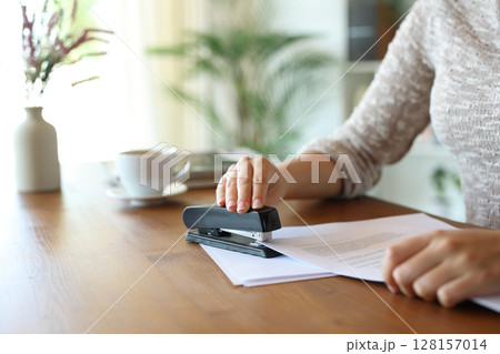 Woman hand stapling papers on a wooden table at home 128157014