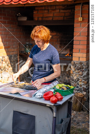Woman seasoning fish and wrapping it in foil for outdoor grilling in her backyard. Homemade cooking, natural ingredients, and traditional barbecue preparation. 128157108