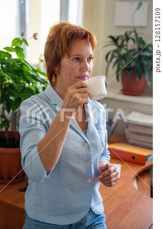 Woman taking a coffee break at her desk in a quiet office setting. Mindful pause, mental reset, and slow work lifestyle. Woman taking a coffee break at her desk in a quiet office setting. Mindful pause, mental reset, and slow work lifestyle. 128157109
