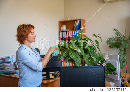 Woman caring for potted plants on her desk during a work break in the office. Slow work, mindful routine, and nature as a source of balance. Woman caring for potted plants on her desk during a work break in the office. Slow work, mindful routine, and nature as a source of balance. 128157112