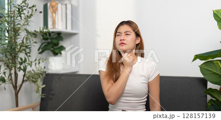 Health Concern: Young woman experiencing throat discomfort while seated. Health Concern: Young woman experiencing throat discomfort while seated. 128157139