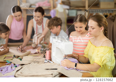Girl child watches female classmates sew and creating clothes Girl child watches female classmates sew and creating clothes 128157662