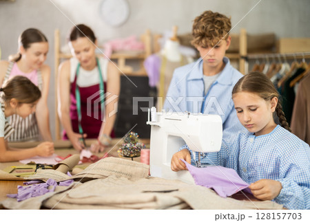 Girl sews on a sewing machine. Boy watches and learns 128157703