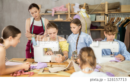 Teenage girl tries to sew surrounded by classmates, female teacher comments and help 128157713
