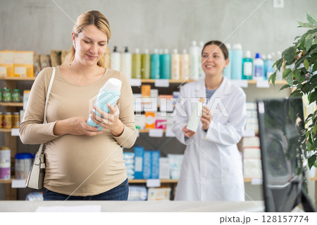Pregnant woman choose shampoo in pharmacy, pharmacist in background offers similar product Pregnant woman choose shampoo in pharmacy, pharmacist in background offers similar product 128157774
