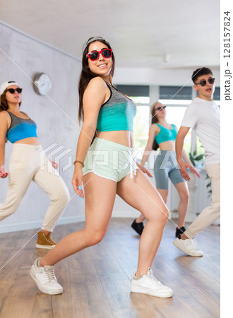 Group of young girls in dark glasses and ball cap and guy dance shuffle in fitness club Group of young girls in dark glasses and ball cap and guy dance shuffle in fitness club 128157824
