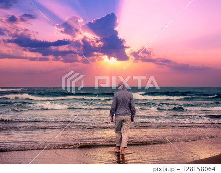 Seascape in the evening with a beautiful sky. A man walks barefoot on the beach and looks at a magical sunset 128158064