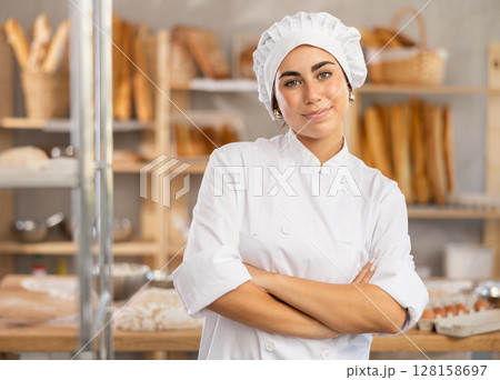 Young female baker stands in bake house, ready to greet customers 128158697