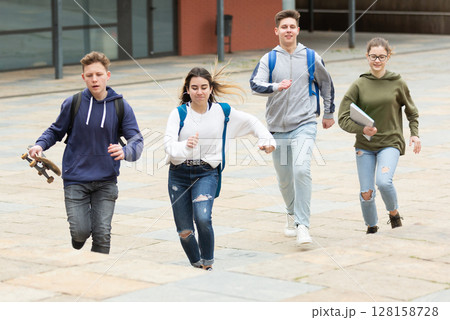 Cheerful teenagers running on city street Cheerful teenagers running on city street 128158728
