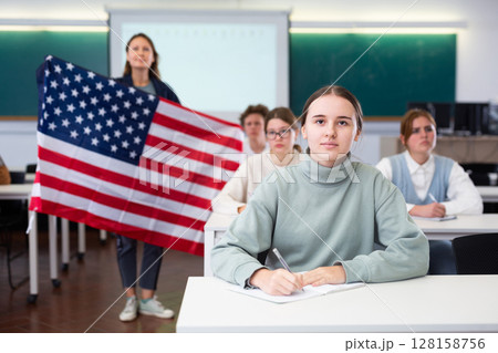 Geography lesson in school class - teacher talks about United States of America, holding flag in his hands Geography lesson in school class - teacher talks about United States of America, holding flag in his hands 128158756