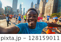 Young man marathon runner taking a selfie while running a marathon, capturing the vibrant atmosphere with a crowd of other runners and the big city skyline in the background, showcasing the excitement 128159011