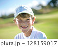 Happy caucasian boy at golfing training lesson, smiling at the camera on a sunny golf course, surrounded by lush green fairways and practicing his swing with enthusiasm, enjoying the sport and 128159017