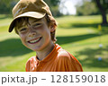 Happy caucasian boy at golfing training lesson, smiling at the camera on a sunny golf course, surrounded by lush green fairways and practicing his swing with enthusiasm, enjoying the sport and 128159018