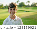 Caucasian boy at a golf training session, happily looking at the camera on a vibrant golf course, engaging in his lesson with eagerness, highlighting the fun and educational aspects of the sport for 128159021