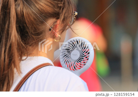 ハンディファンを持って歩く女性 128159154