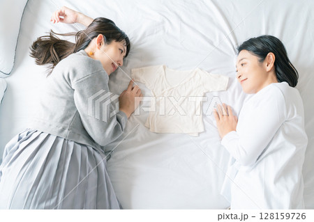 ベッドに寝転び肌着を挟んで赤ちゃんが待ち遠しい母と娘 128159726