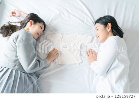 ベッドに寝転び肌着を挟んで赤ちゃんが待ち遠しい母と娘 128159727