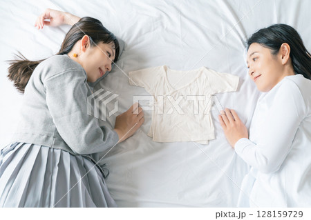 ベッドに寝転び肌着を挟んで赤ちゃんが待ち遠しい母と娘 128159729