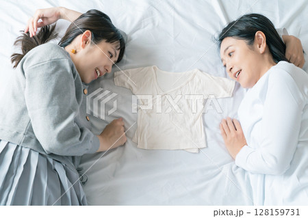 ベッドに寝転び肌着を挟んで赤ちゃんが待ち遠しい母と娘 128159731