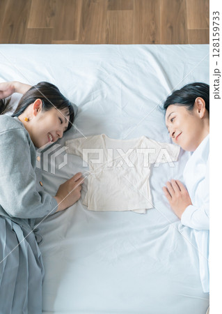 ベッドに寝転び肌着を挟んで赤ちゃんが待ち遠しい母と娘 128159733