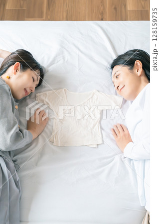 ベッドに寝転び肌着を挟んで赤ちゃんが待ち遠しい母と娘 128159735