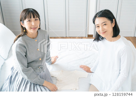 寝室で赤ちゃんの服を準備する母と娘 寝室で赤ちゃんの服を準備する母と娘 128159744