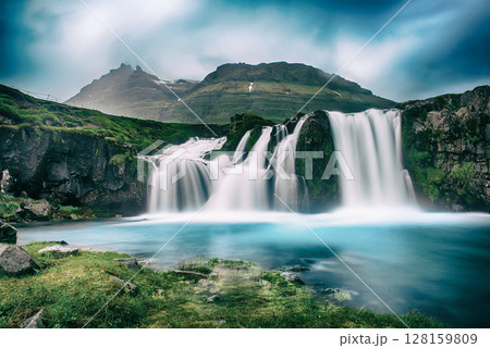 View to the Kirkjufell waterfall at summer. Kirkjufellsfoss waterfall, Iceland, Europe. View to the Kirkjufell waterfall at summer. Kirkjufellsfoss waterfall, Iceland, Europe. 128159809