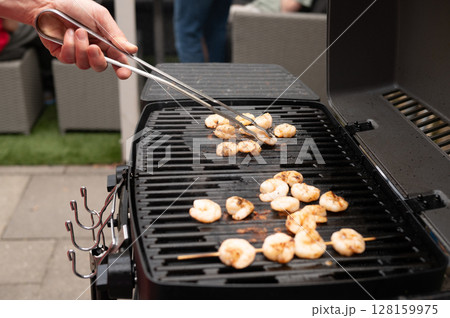 Grilled shrimp on outdoor barbecue with tongs in backyard setting 128159975