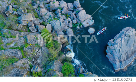 Aerial view of two kayaks navigating through a narrow rocky river pass surrounded by large boulders and lush vegetation in a scenic natural landscape 128160272