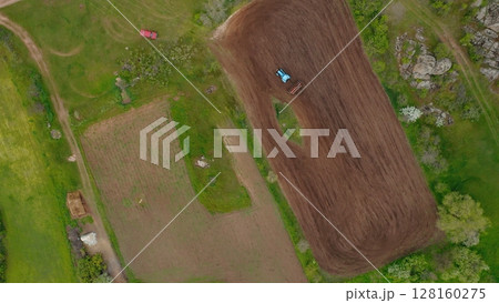 Aerial view of a tractor planting a field on a small plot of fertile land. Heavy machinery when sowing, working in the fields. Aerial view of a tractor sowing land in a field. 128160275