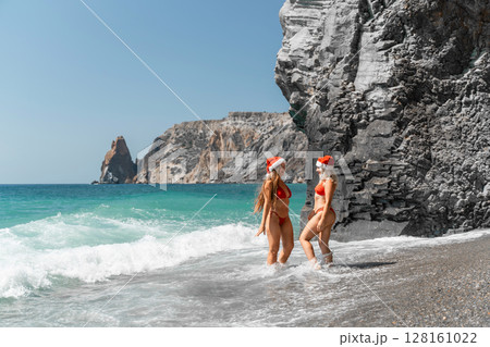 Women in Santa Claus hats run into the sea dressed in red swimsuits. Celebrating the New Year in a hot country Women in Santa Claus hats run into the sea dressed in red swimsuits. Celebrating the New Year in a hot country 128161022