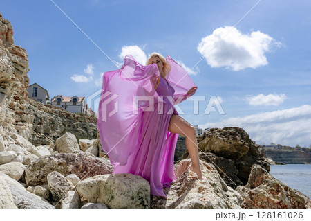 Model fashion rock Woman poses with purple dress on beach at daytime for photoshoot Model fashion rock Woman poses with purple dress on beach at daytime for photoshoot 128161026