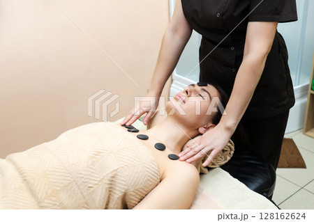 Woman with hot stones placed on her chest relaxes in a massage parlor Woman with hot stones placed on her chest relaxes in a massage parlor 128162624