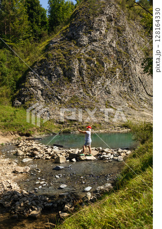 Senior Woman Walking Across Stones by Mountain Pond Senior Woman Walking Across Stones by Mountain Pond 128164330