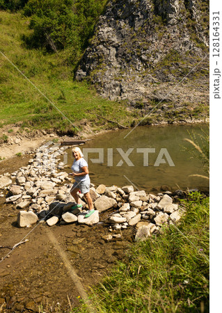 Senior Woman Walking Across Stones by Mountain Pond 128164331