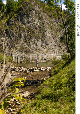 Senior Woman Walking Across Stones by Mountain Pond 128164333