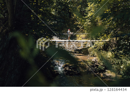 Person Standing on Small Bridge in Lush Forest 128164434