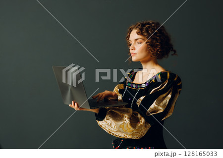 Portrait of a young aristocratic woman dressed in a medieval dress working on laptop 128165033