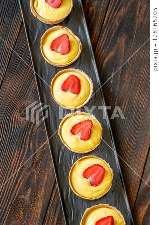 Mini mango cream tarts topped with strawberries lined on elegant black plate 128165205