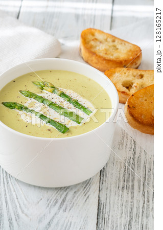 Creamy asparagus soup in white bowl with swirl and toasted ciabatta 128165217