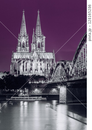 Cologne, Germany. Night View Of Cologne Cathedral And Hohenzollern Bridge. Catholic Gothic Cathedral In Night Lighting. UNESCO. Black, White And Ultra Violet Colors Cologne, Germany. Night View Of Cologne Cathedral And Hohenzollern Bridge. Catholic Gothic Cathedral In Night Lighting. UNESCO. Black, White And Ultra Violet Colors 128165286