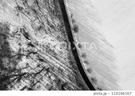 Droning above a winter landscape shows a mix of snow-covered fields and bare trees. Shadows stretch across the land, enhancing the serene beauty of the cold season. Droning above a winter landscape shows a mix of snow-covered fields and bare trees. Shadows stretch across the land, enhancing the serene beauty of the cold season. 128166167