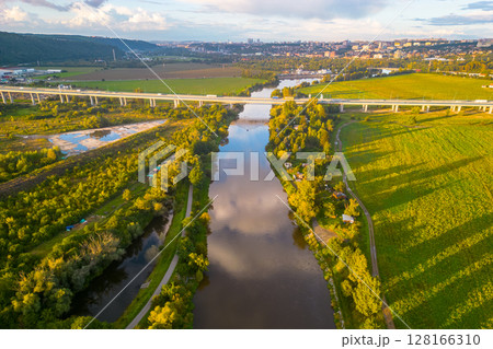 An aerial view of the Lahovice Bridge spanning the Berounka River, surrounded by lush greenery under a cloudy sky. Prague, Czechia 128166310