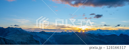 Colors blend beautifully as the sun sets behind a rugged mountain range. The sky transforms into hues of orange and pink, casting a serene glow over the peaks and valleys below. Colors blend beautifully as the sun sets behind a rugged mountain range. The sky transforms into hues of orange and pink, casting a serene glow over the peaks and valleys below. 128166317