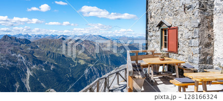 A tranquil scene at the Julius Payer House, showcasing a terrace with wooden benches and tables, affording visitors breathtaking views of the Italian Eastern Alps. Ortles Mountain, Italy 128166324