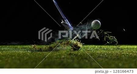 Golf club hitting ball off turf with dirt and grass flying in dark background 128166473