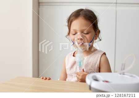 cute little toddler girl inhaling medicine on nebulizer and holding it on her own 128167211