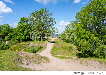 A tranquil pathway winds through lush greenery at Battery Park on Vaxholm Island near Stockholm. Visitors enjoy outdoor activities surrounded by vibrant nature and scenic views of the water. A tranquil pathway winds through lush greenery at Battery Park on Vaxholm Island near Stockholm. Visitors enjoy outdoor activities surrounded by vibrant nature and scenic views of the water. 128167324