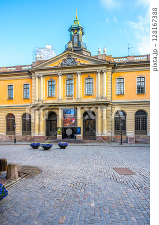 The Nobel Prize Museums facade stands prominently in Stockholm, Sweden, its entrance adorned with flags under a clear sky. The Nobel Prize Museums facade stands prominently in Stockholm, Sweden, its entrance adorned with flags under a clear sky. 128167388