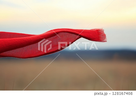 Flowing red scarf dances in the wind against a serene landscape at sunset Flowing red scarf dances in the wind against a serene landscape at sunset 128167408